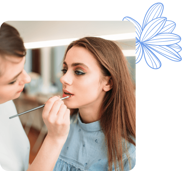 Una persona aplicando lápiz labial a otra, que está mirando hacia el frente mientras se le maquilla los labios.