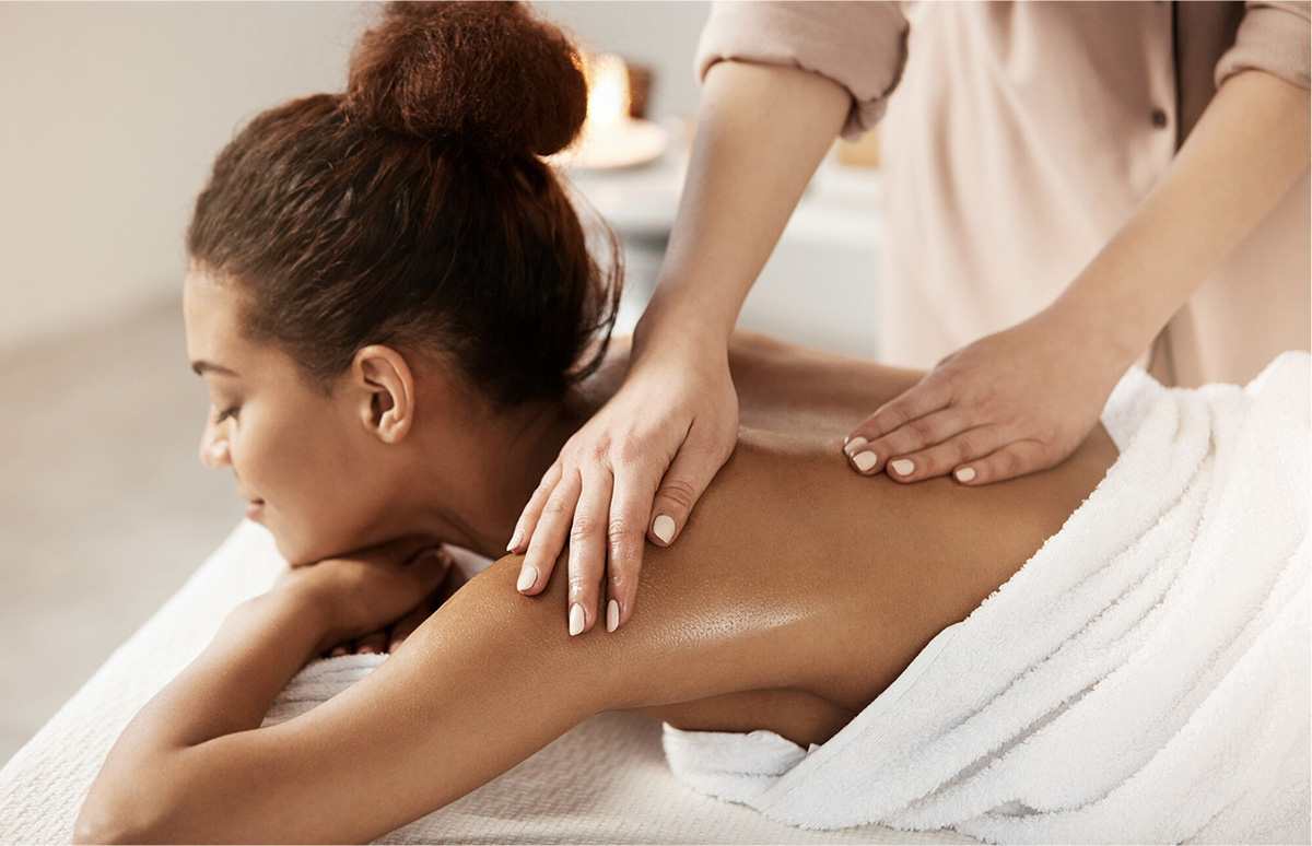 Mujer recibiendo un masaje en la espalda mientras está acostada sobre una mesa de tratamiento, con una toalla envuelta alrededor de su cuerpo.