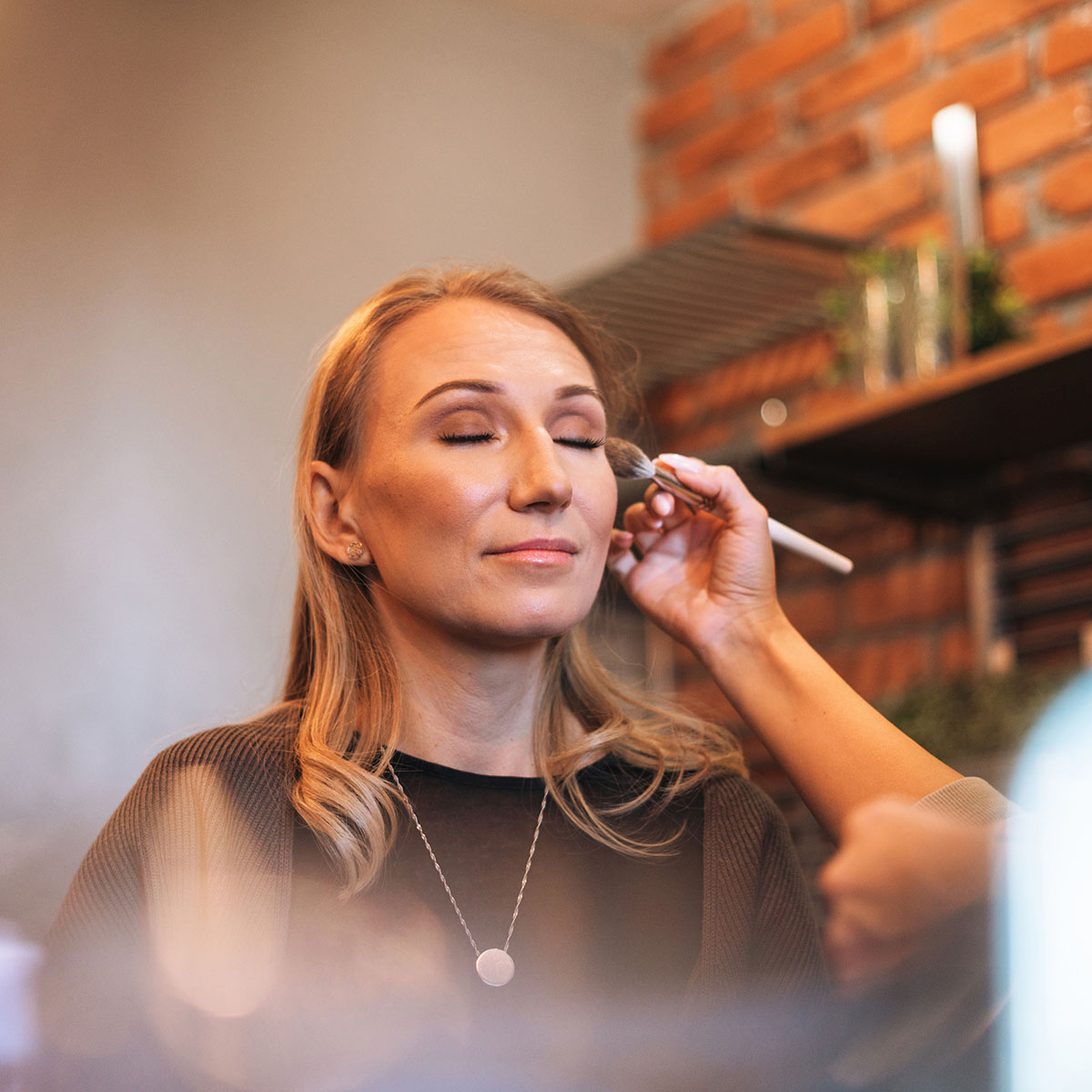 Maquilladora aplicando polvos en el rostro de una clienta, destacando los servicios de maquillaje profesional del centro.