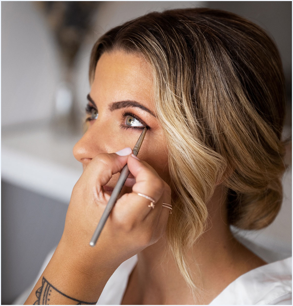 Una persona está aplicando lápiz de ojos en el párpado inferior de una mujer mientras se observa su mirada atenta.