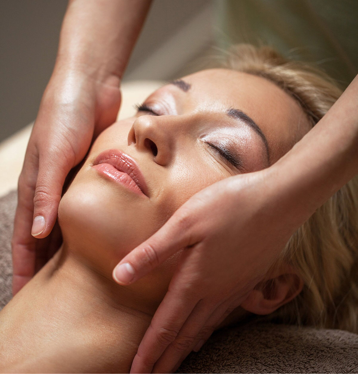 Mujer recibiendo un masaje facial relajante, con un profesional sujetando suavemente su rostro.