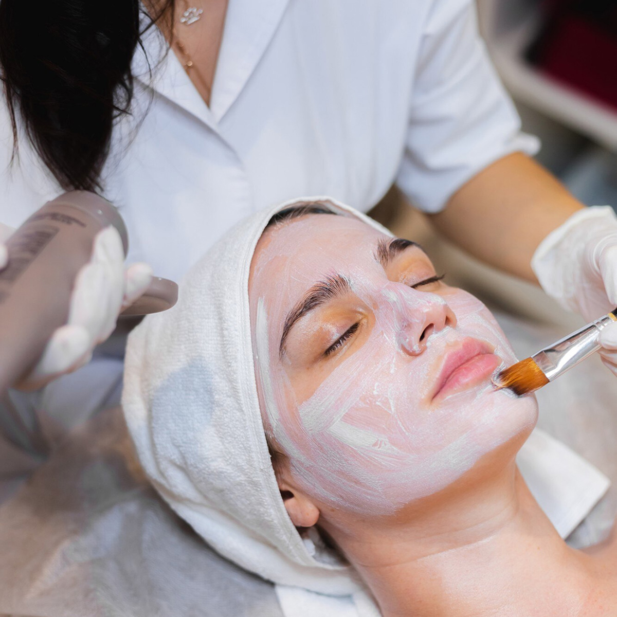 Aplicación de mascarilla facial a una clienta, destacando el enfoque del centro en el cuidado y la estética de la piel.