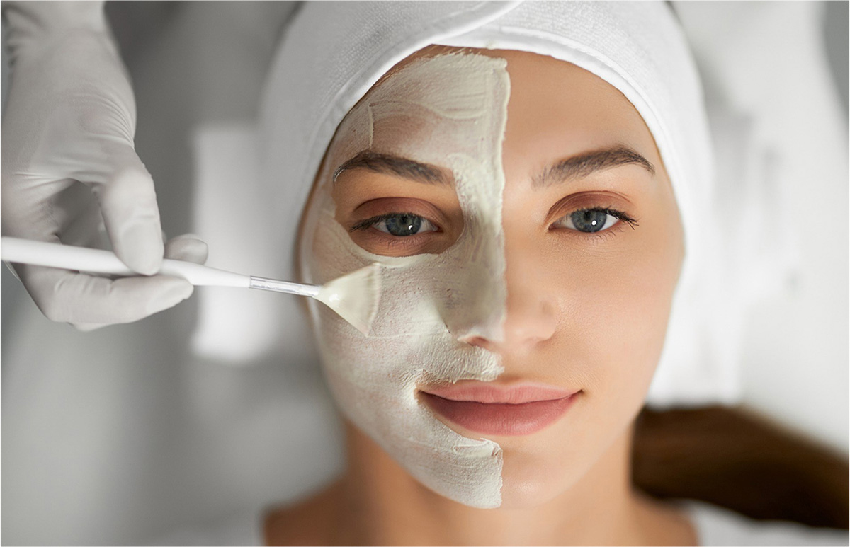 Mujer recibiendo un tratamiento facial, con una máscara de crema aplicada en mitad de su rostro.